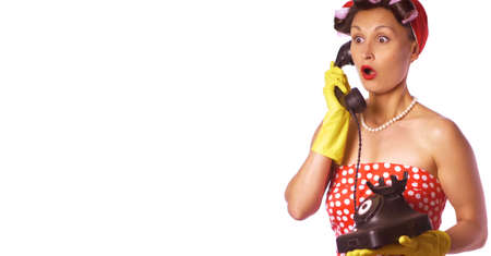 Wow face. Amazed housewife in pin up style speaks on the phone. Retro lady in a red dress and a yellow household gloves. Housework or cleaning concept.の写真素材