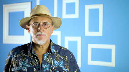 Studio portrait of an fashion old man in summer hawaiian shirts and straw hat looking at camera on a...