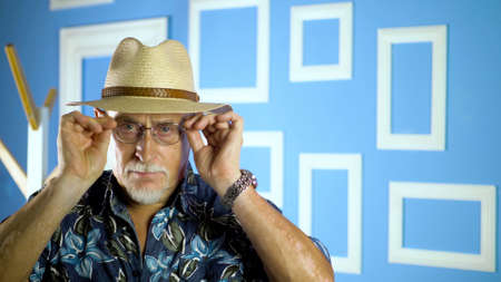 Studio portrait of an fashion old man in summer hawaiian shirts and straw hat looking at camera on a colorful wall.の写真素材
