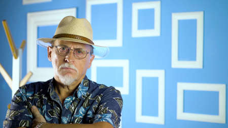Studio portrait of an fashion old man in summer hawaiian shirts and straw hat looking at camera on a colorful wall.の写真素材