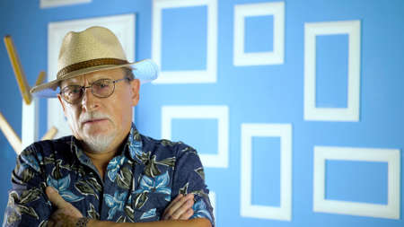 Studio portrait of an fashion old man in summer hawaiian shirts and straw hat looking at camera on a colorful wall.の写真素材