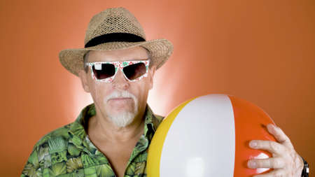 Studio portrait of the joyful elderly tourist in a straw hat and hawaiian shirt on colored backgrounds. Peoples emotion. Happy and funny celebrating people.の写真素材