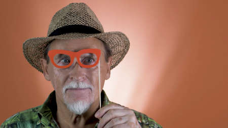 Studio portrait of the joyful elderly tourist in a straw hat and hawaiian shirt on colored backgrounds. Peoples emotion. Happy and funny celebrating people.の写真素材