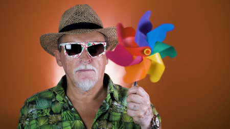Studio portrait of the joyful elderly tourist in a straw hat and hawaiian shirt on colored backgrounds. Peoples emotion. Happy and funny celebrating people.の写真素材