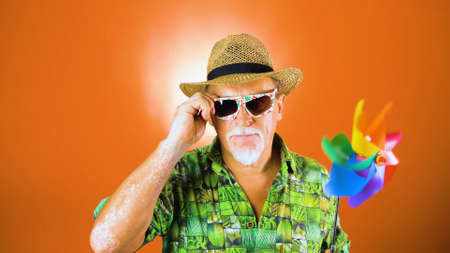 Studio portrait of the joyful elderly tourist in a straw hat and hawaiian shirt on colored backgrounds. Peoples emotion. Happy and funny celebrating people.の写真素材