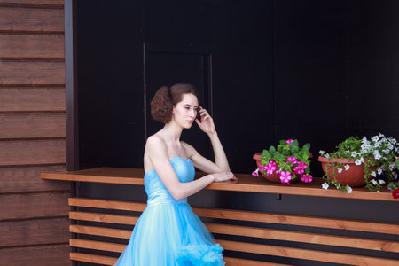 Russia, Izhevsk - June 21, 2017:Young girl is standing by the wooden desk in a beautiful blue dress. Summer morning.のeditorial素材