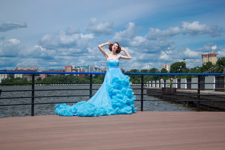 Russia, Izhevsk - June 21, 2017:Young woman is standing on a pier in a beautiful blue dress. Bright sunny day.のeditorial素材