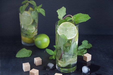 Two glasses of mojito cocktail with fresh lime and mint on a dark background. Ice cubes and pieces...