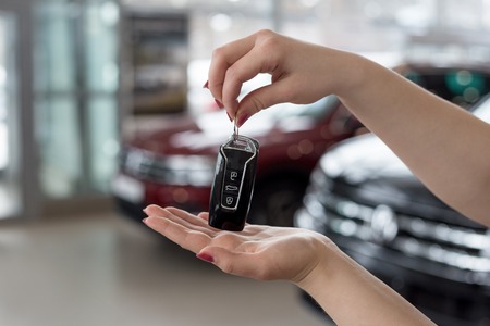 Dealer woman is holding in her hands the keys to the new car. Modern and prestigious vehicles. For...