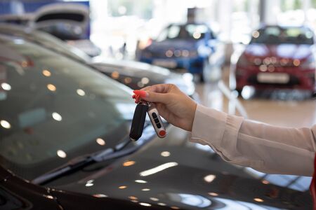 Dealer woman holding keys to a new car. Modern and prestigious vehicles. For use as a background.