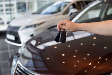 Salesperson holding keys to a new car. Modern and prestigious vehicles. For use as a background.