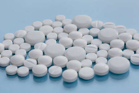 Pile of white pills isolated on a on blue background. Medical health or drugs addiction concept. Copy space for you text.の写真素材