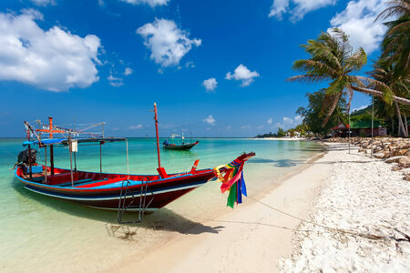 The sea coast with turquoise water, wooden boats and palm trees ashore.の写真素材