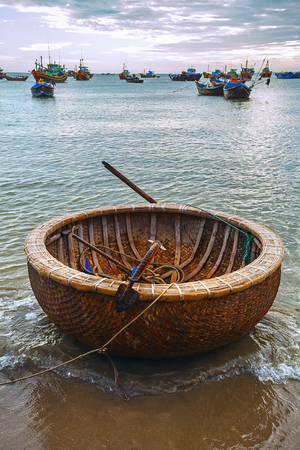 National round wicker boat on the beach. Sea sunset and the fishing boats.の写真素材