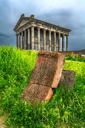 The temple of Garni. In the foreground is a carved stone with Christian symbols in the green grass.の写真素材