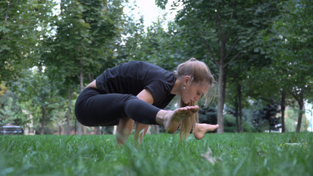 Young girl practicing yoga in the park on the green grass. Early autumn. In the grass are yellow leaves. The girl is young and healthy.の写真素材