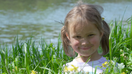 Portrait of a smiling little girl. Baby girl sitting in tall grass. Tiny kid have fun, enjoy nature outdoors.の写真素材