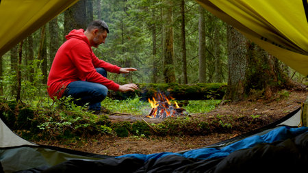 Bearded man by the fire in a beautiful forest. The camping is located in a beautiful forest lawn in the mountains. Travel conceptの写真素材