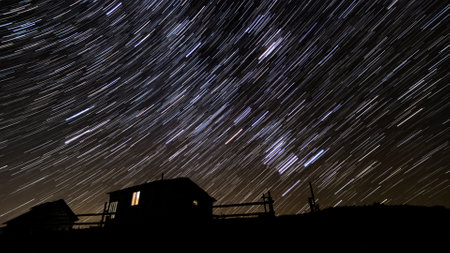 Wooden house in the mountains in winter. Star trails in the night sky.