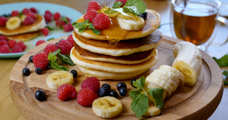 Sweet honey pouring over pancakes. Tasty breakfast food. Pancakes are served with raspberries, banana and mint leaf. Honey dripping down on dessertの写真素材
