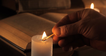Lighting a candle. Old book on the table. Reading and teaching by candlelight at night.の写真素材