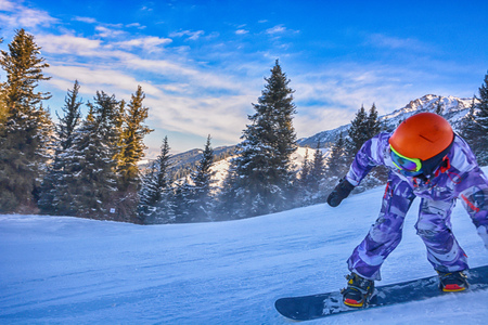 Young man snowboarder running down the slope in Karakol mountains. Beautiful sunny day snowboarding closeup.の写真素材