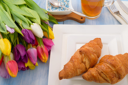 bright tulips, tea with lemon, kruassant on a white plateの写真素材