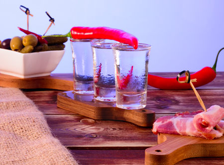 Shots of vodka, bacon, olives and pickles on a wooden tableの写真素材