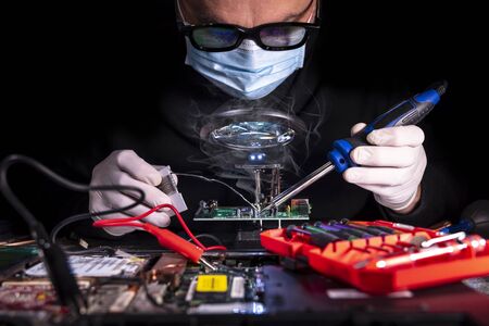 Hands of a man in white gloves repair laptop using soldering iron. Man repairing broken computer, video card,memory, RAM, cooler, processor,hard drive.の写真素材