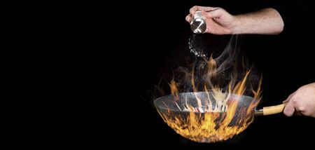 The chef adds salt to the food cooked in a pan over very high heat.の写真素材