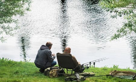 A fisherman catches fish on the river on a warm spring day. A man catches fish sitting on a chair.の写真素材