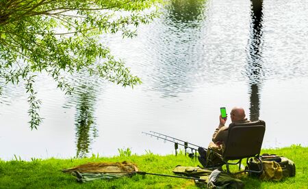 A fisherman is talking on the smartphone while fishing.Smartphone with green screenの写真素材