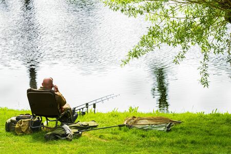 A fisherman catches fish on the river on a warm spring day. A man catches fish sitting on a chair.の写真素材
