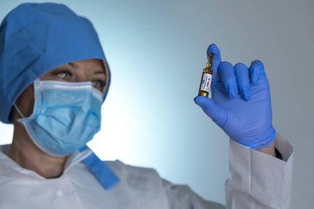 Doctor  in medical mask  holds in hand  ampoule with vaccine against coronavirus. A medicine against a coronavirus COVID-19. Ready antiviral vaccine in ampoules to be appliedの写真素材