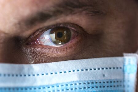 Tears in eyes of crying male doctor in mask. Face close-up. Pandemic and virus epidemic. Coronavirus covid-19. Tears in eyes.の写真素材
