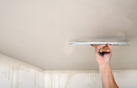 Hand of builder worker spacks ceiling with putty plaster aligning ceiling with spatula. Renovation and construction worksの写真素材