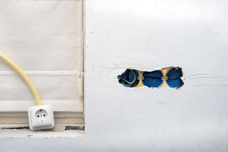 Electrical wire and opened junction box on plastering wall. Home renovation concept