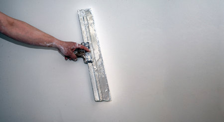 Hand of builder worker spacks wall with putty plaster aligning wallwith spatula. Renovation and...