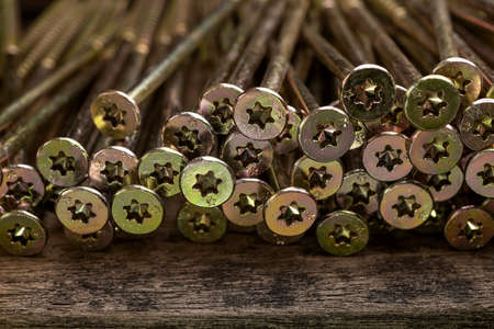 Close up shooting of parts of carpentry screws with cross head. Yellow screws on the table. Industry...