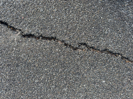 Close-up of a cracked asphalt surface with small green grass sprouting from the crackの写真素材