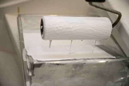 Close-up of a roller soaked in white paint on a ribbed plastic tray. Concept for renovation, paint preparation, and DIY interior renovation.の写真素材