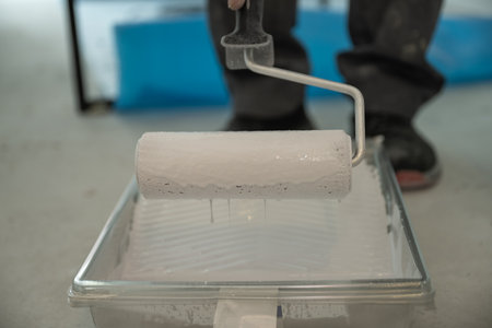 Close-up of a roller soaked in white paint on a ribbed plastic tray. Concept for renovation, paint preparation, and DIY interior renovation.の写真素材