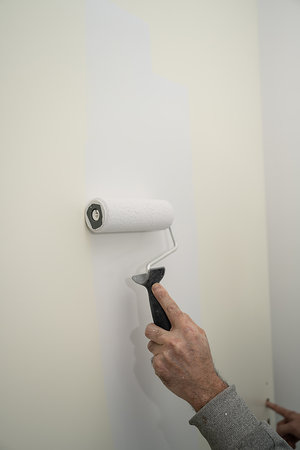 A person painting an interior wall with roller, applying a fresh white coat over a beige surface.の写真素材
