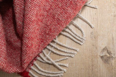 Red woven throw with tassels on a rustic wooden floor. Soft texture, cozy home decor moodの写真素材