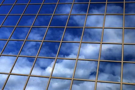 a mirror reflection of sky and clouds is in the windows of buildingの写真素材