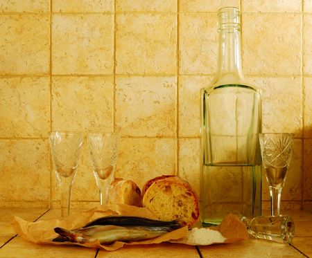 Transparent liquid in a bottle, wineglasses, bread and salt on a tiled backgroundの写真素材