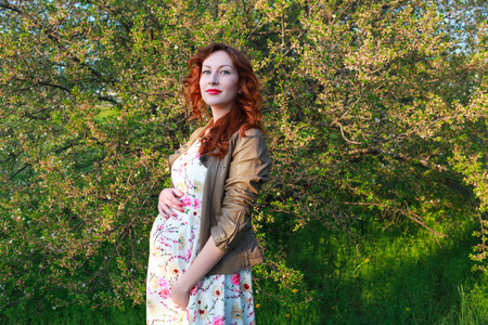 Beautiful pregnance woman near the cherry blossom branch. Red hair and lips. Mother and babyの写真素材