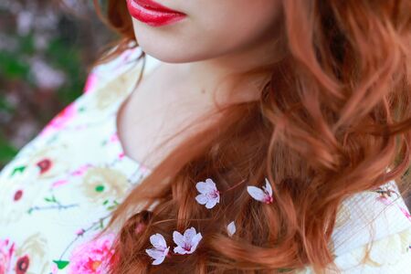 portrait of beautiful woman near the cherry blossom branch. Purple flowers in red hair. Lips.の写真素材