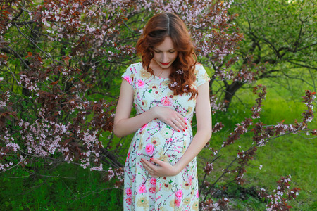 Beautiful pregnance woman near the cherry blossom branch. Red hair, lips. Mother and babyの写真素材