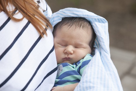 Newborn baby is sleeping on mothers hands in slingの写真素材